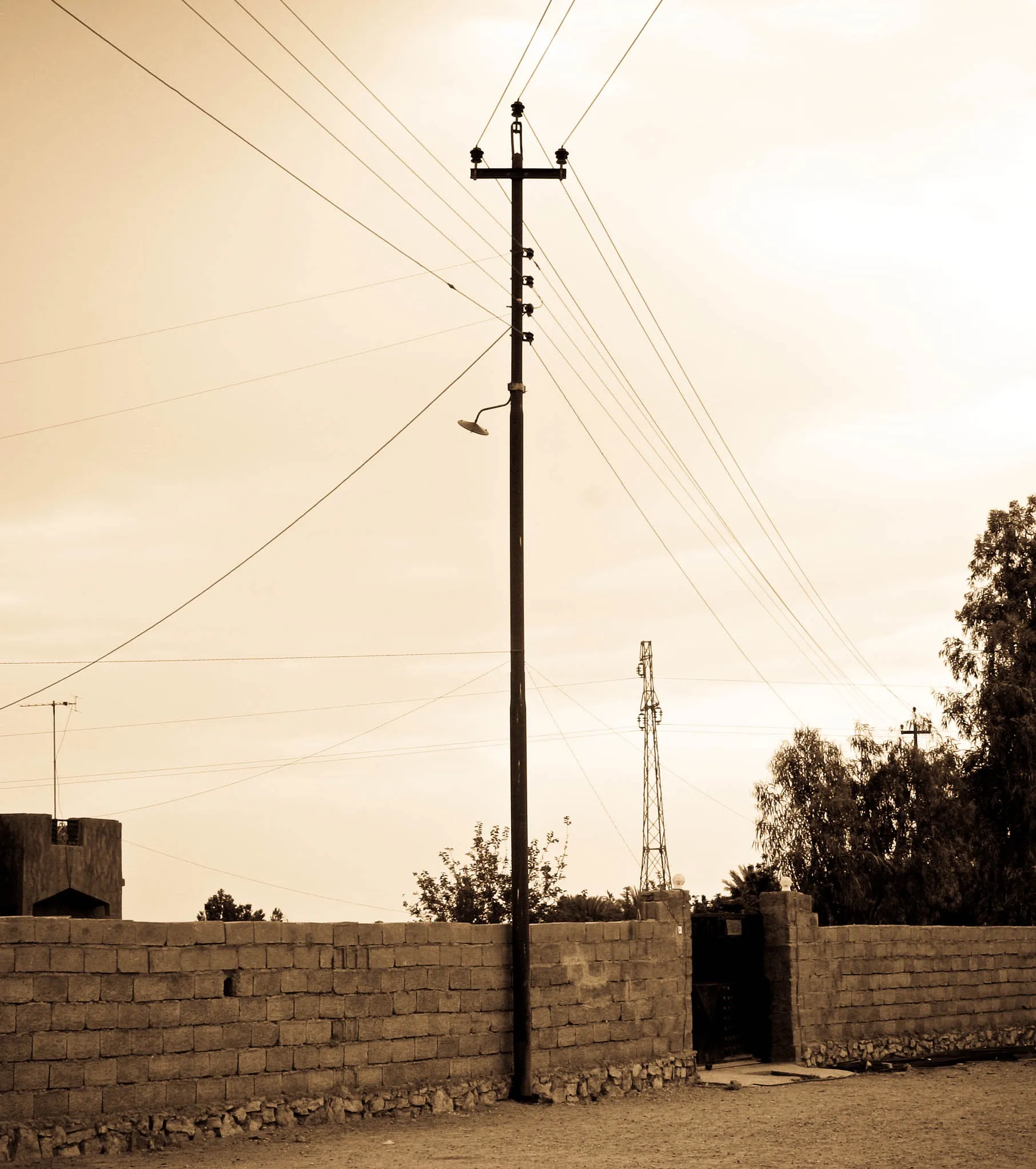 Sepia-toned image of a tall utility pole and converging wires above a low masonry wall.