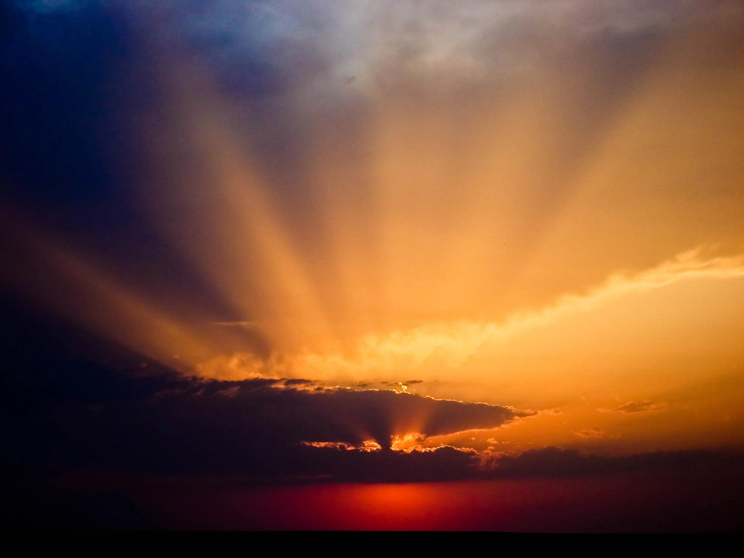 Orange sunlight streams through a break in dark clouds above a red horizon.