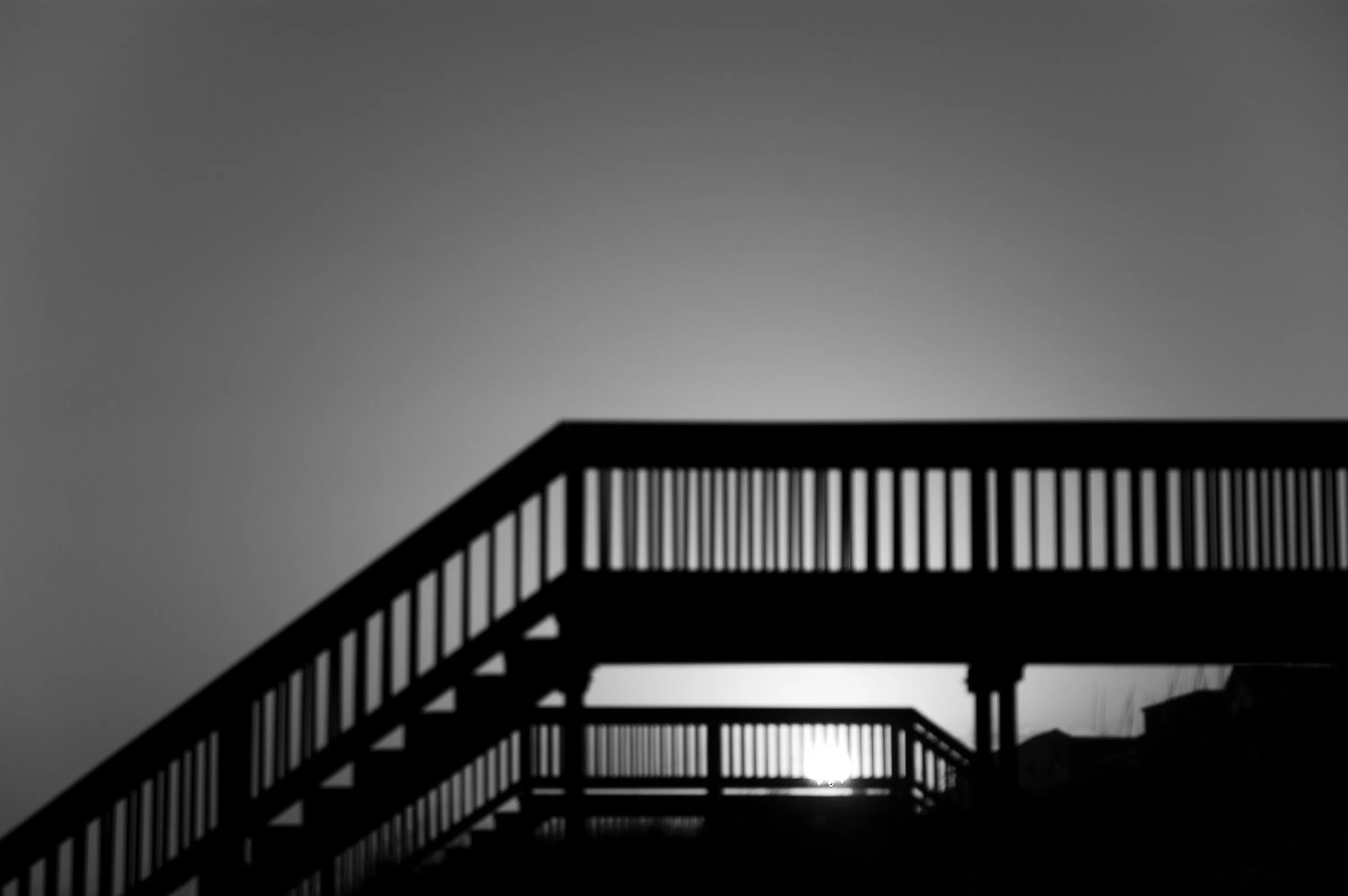Dark stair railings form diagonal bands against a softly blurred sky and low sun.