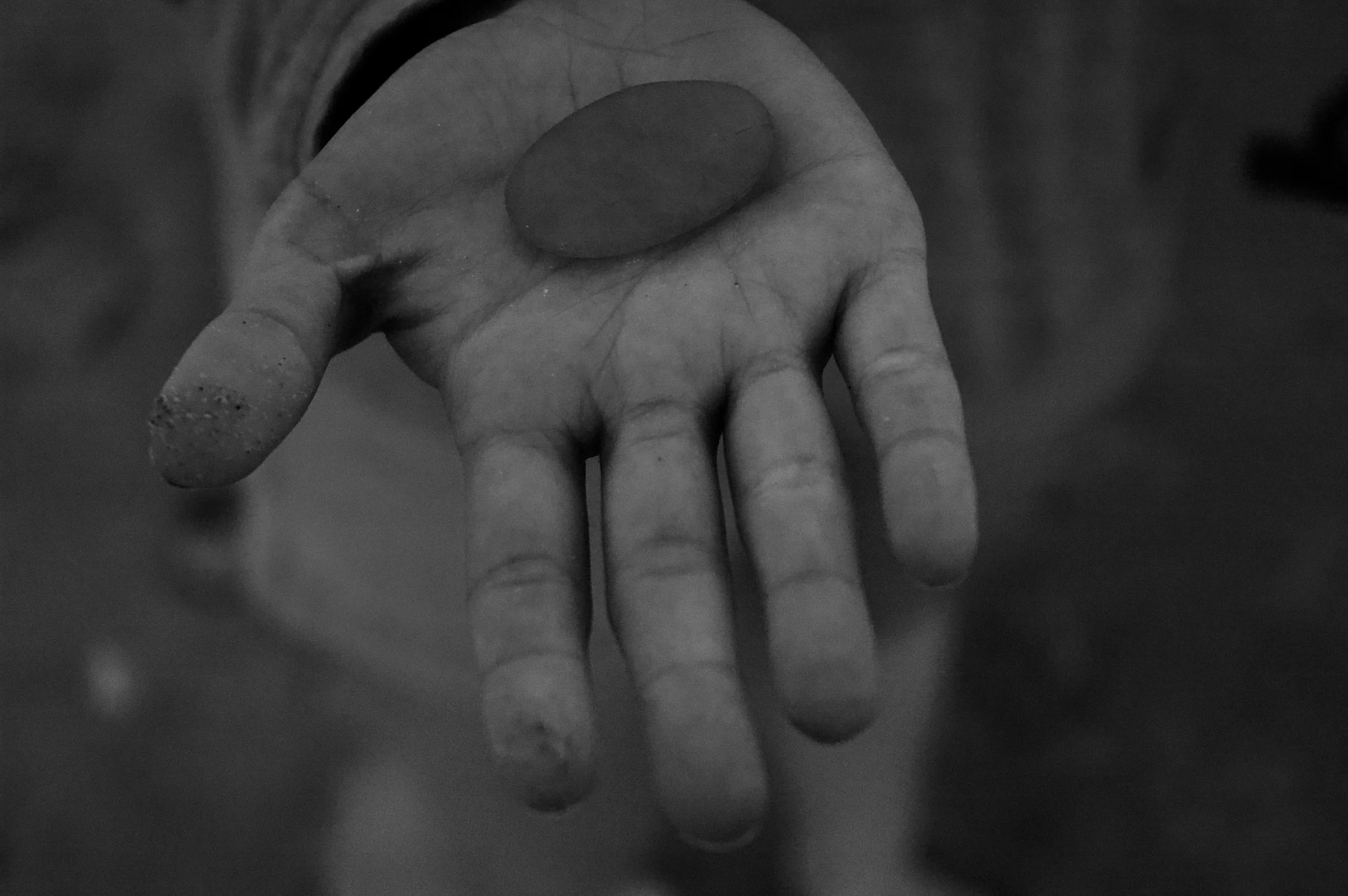 Close-up of an open hand holding a small smooth oval stone above shallow water.