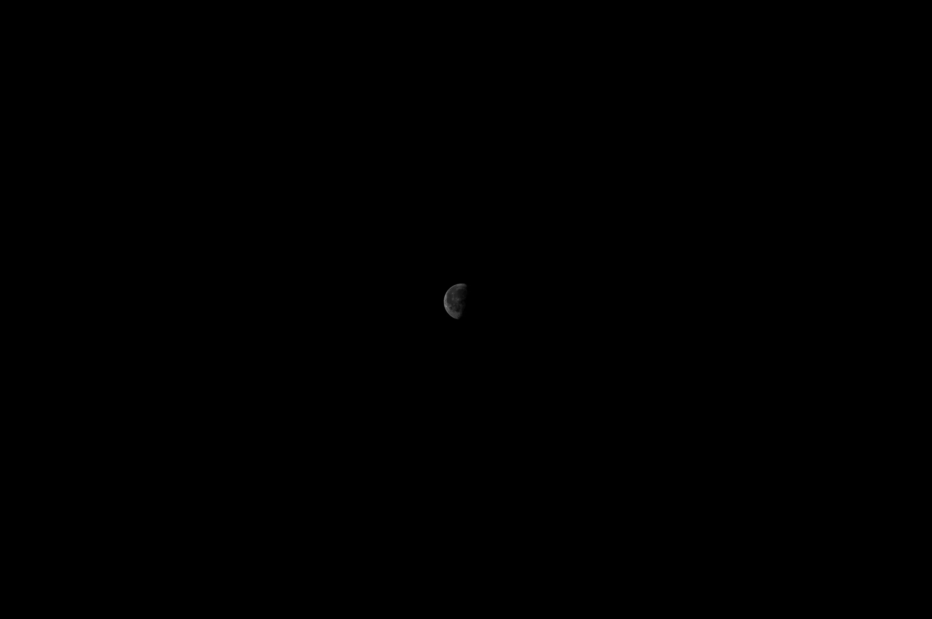 A small pale moon appears near the center of a deep blue sky.