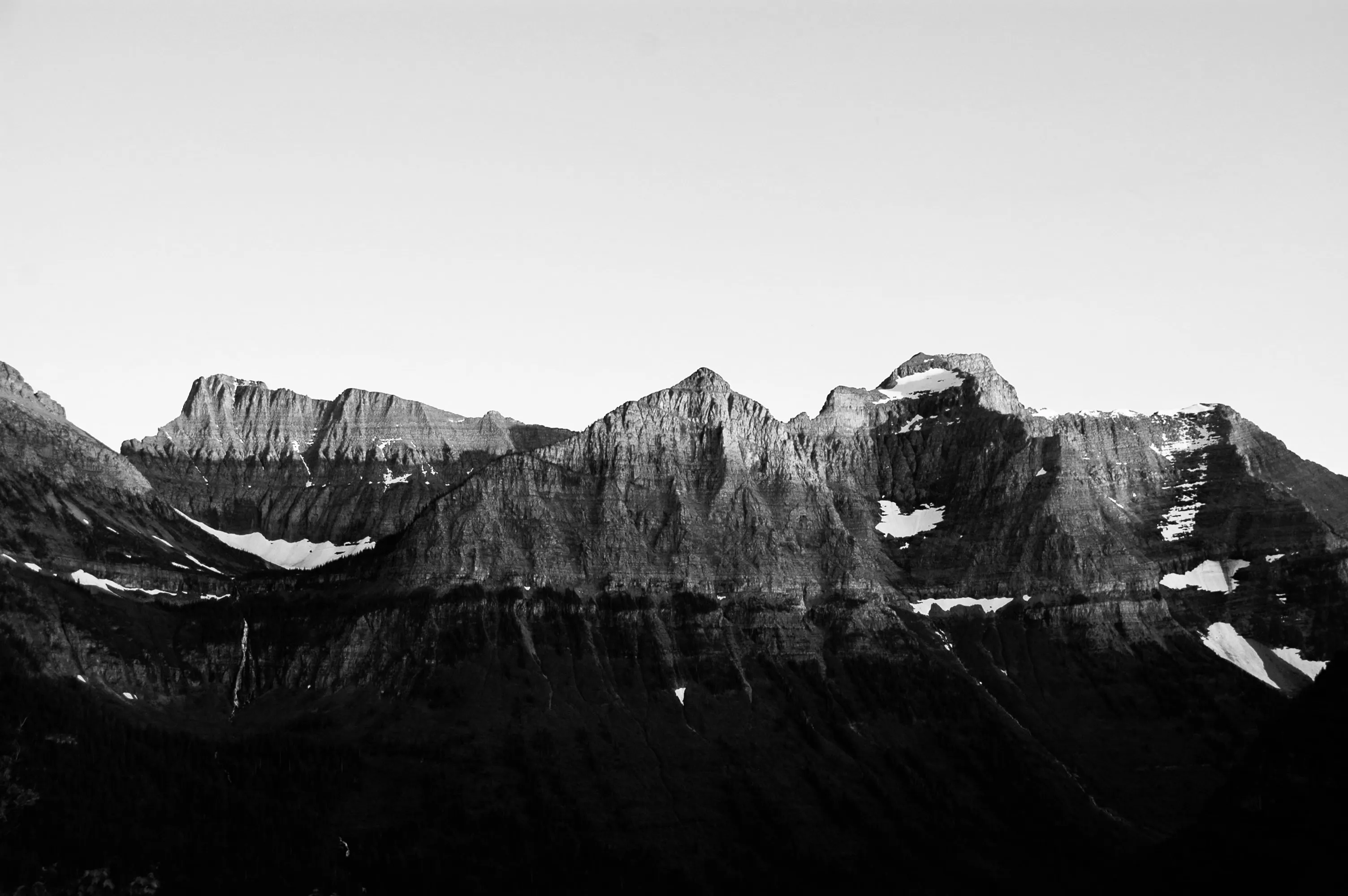 Black-and-white view of a jagged mountain ridge with patches of snow above a very dark valley.