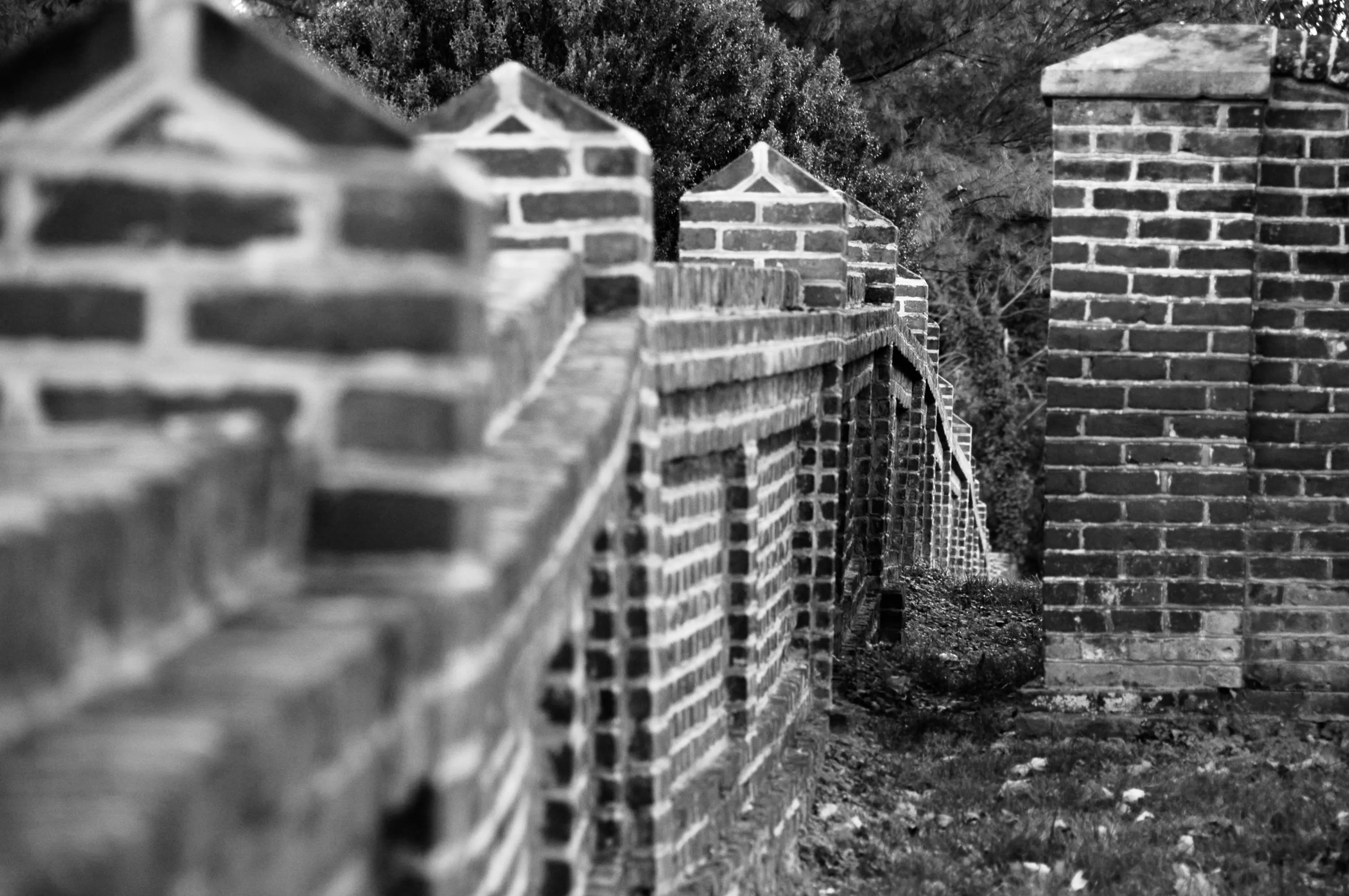 Black-and-white close view of a brick wall receding into the distance through repeated square brick piers.