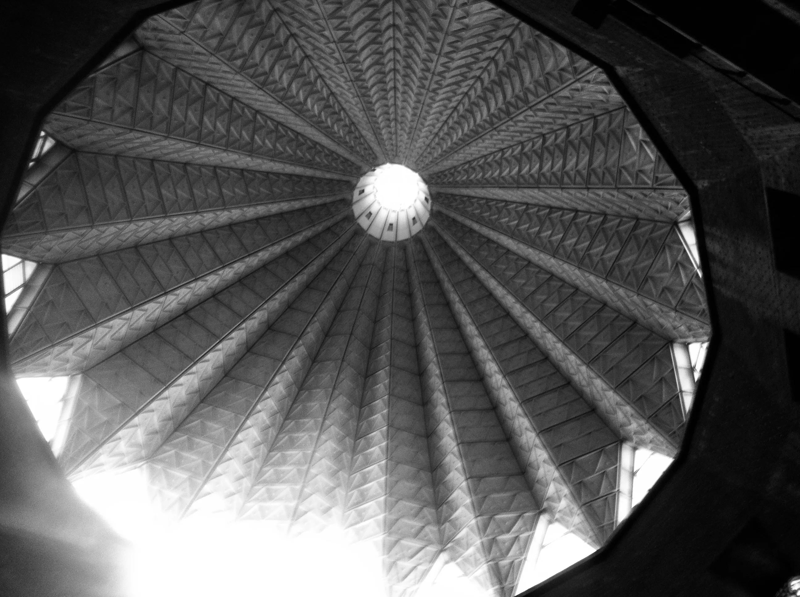 Black-and-white upward view of a circular roof with radiating patterned panels converging at a bright skylight.