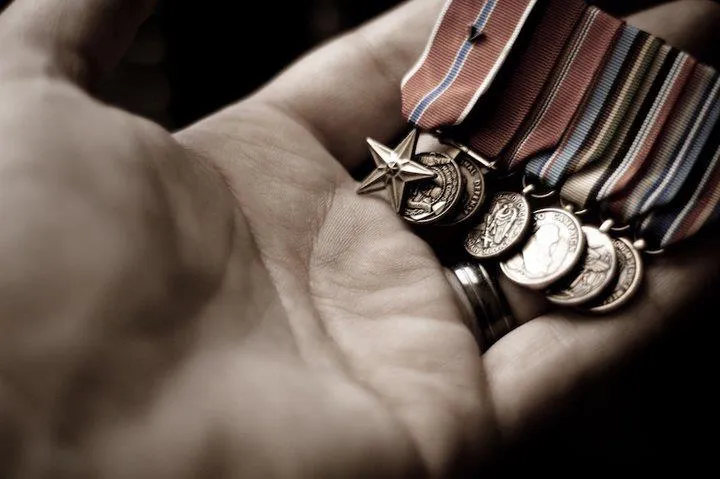 Close-up photograph of an open hand holding several metal medals attached to striped ribbons.