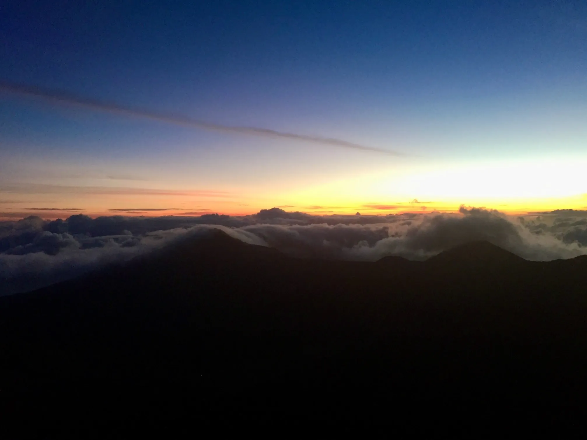 A blue and orange sunrise over dark mountain ridges and clouds, viewed from above.