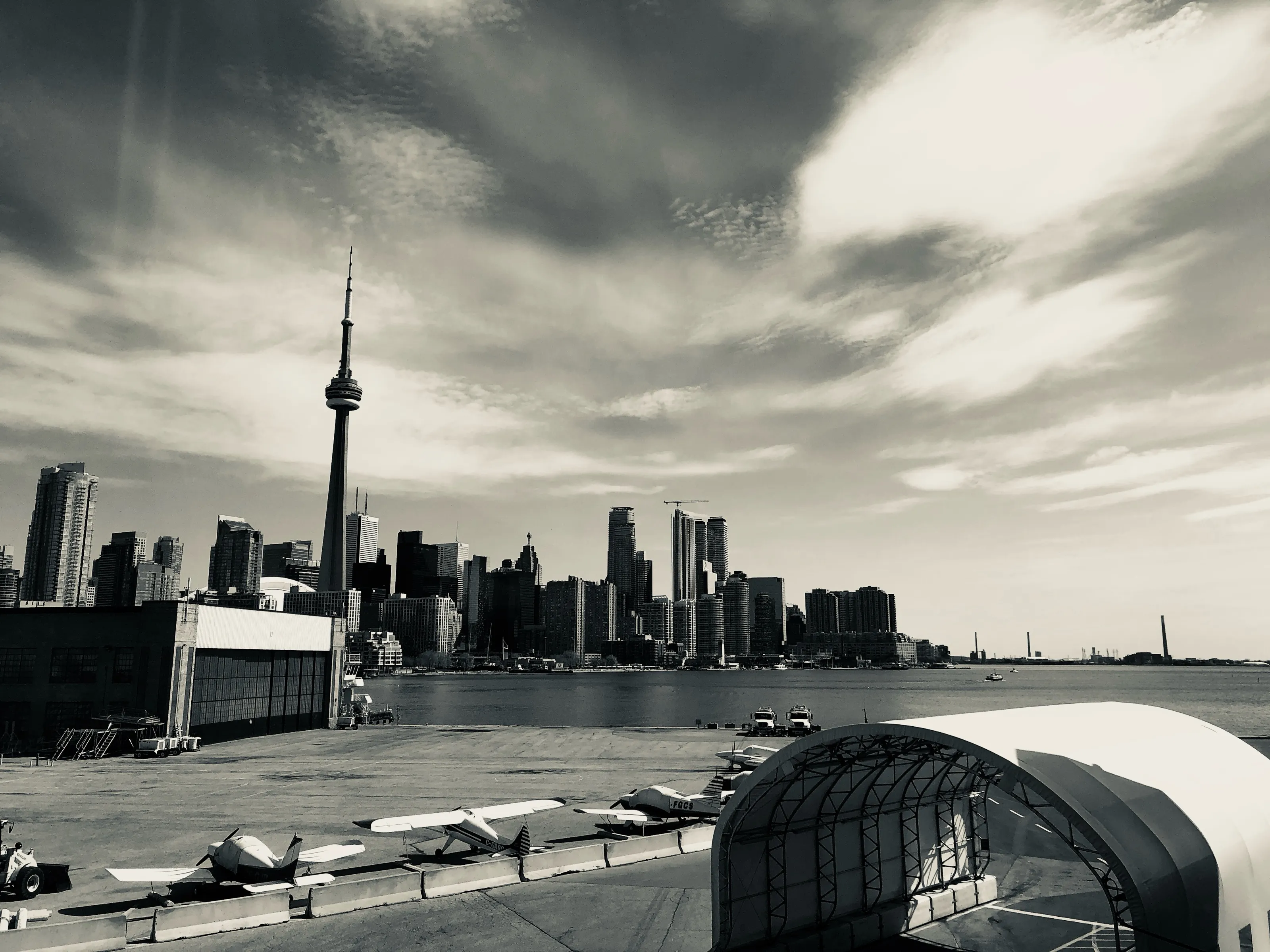 Black-and-white view of a waterfront city skyline with a tall communications tower and small planes in the foreground.