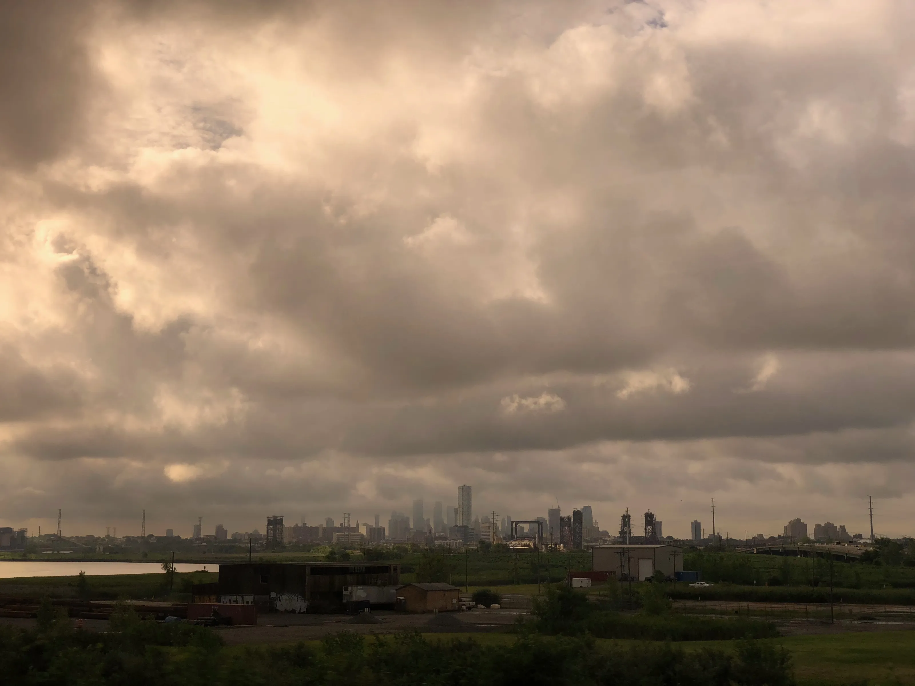 Dark storm clouds over a distant city skyline, rail lines, and low industrial buildings.