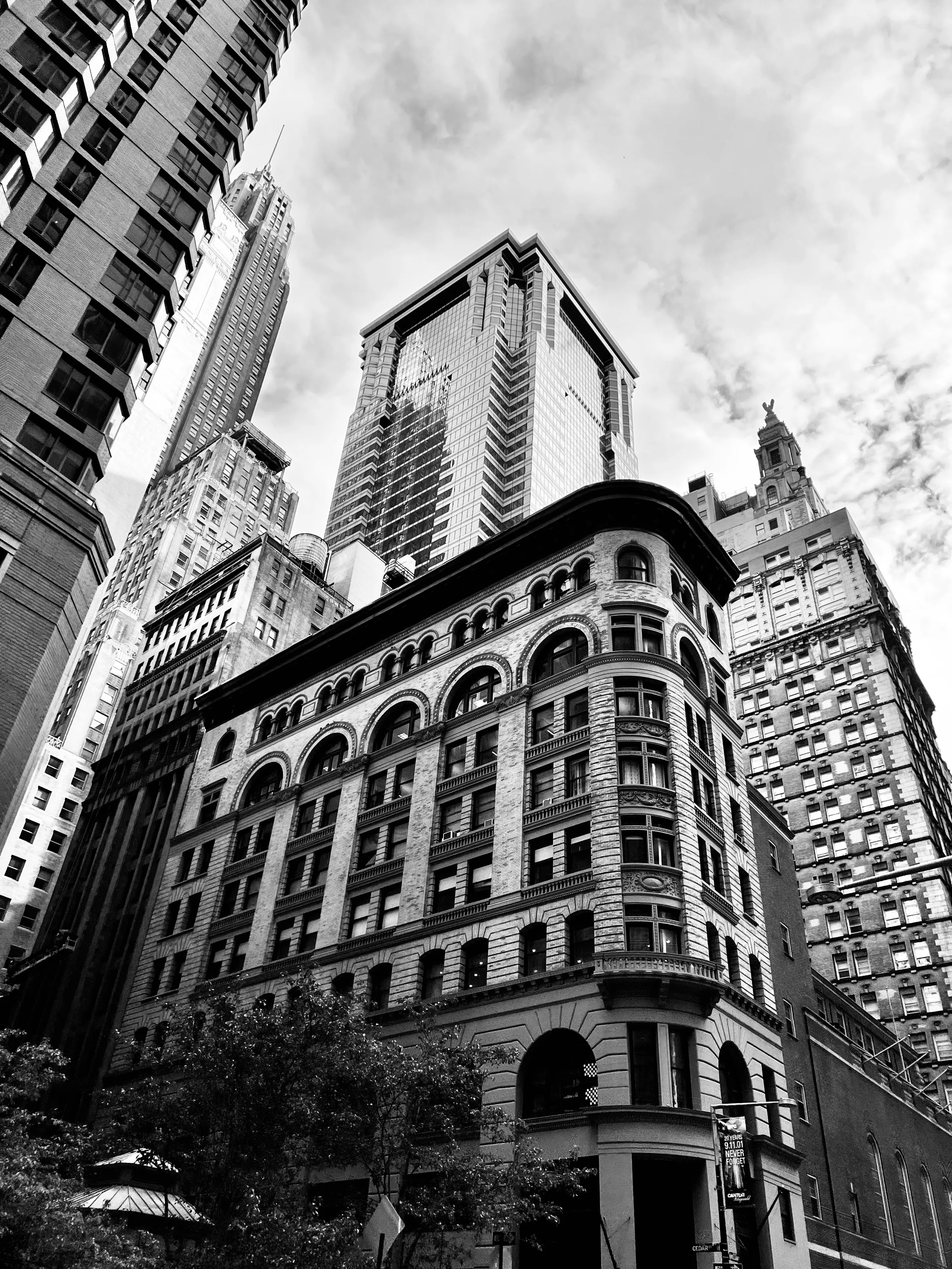 Black-and-white low-angle view of a rounded historic stone building surrounded by taller city skyscrapers.
