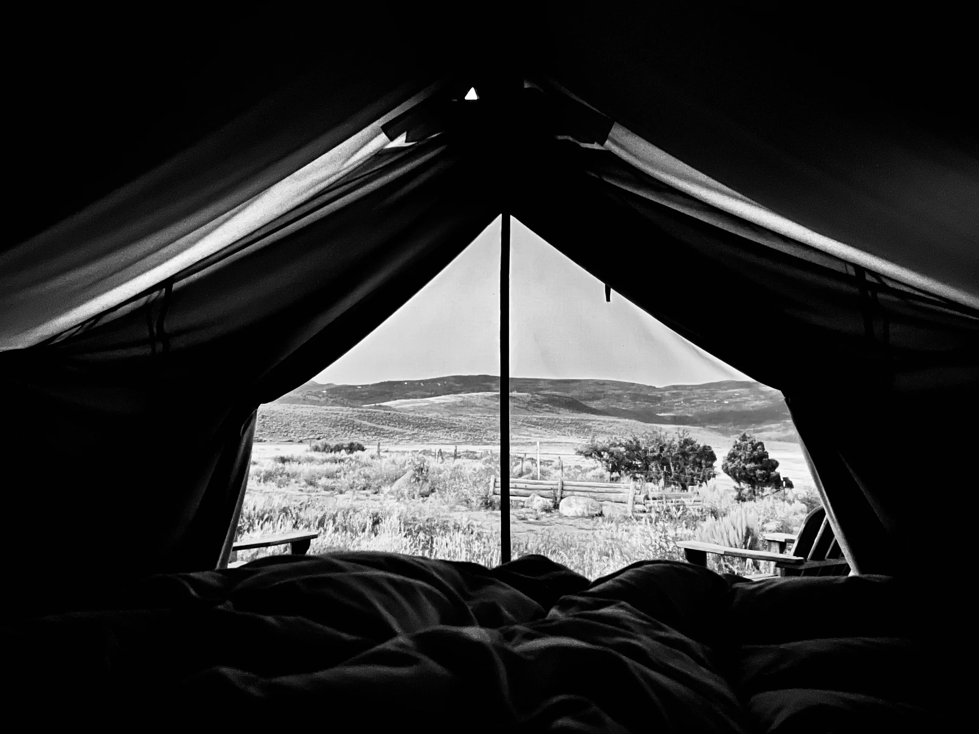 View from inside a dark tent, with its triangular opening framing grassland and low hills.