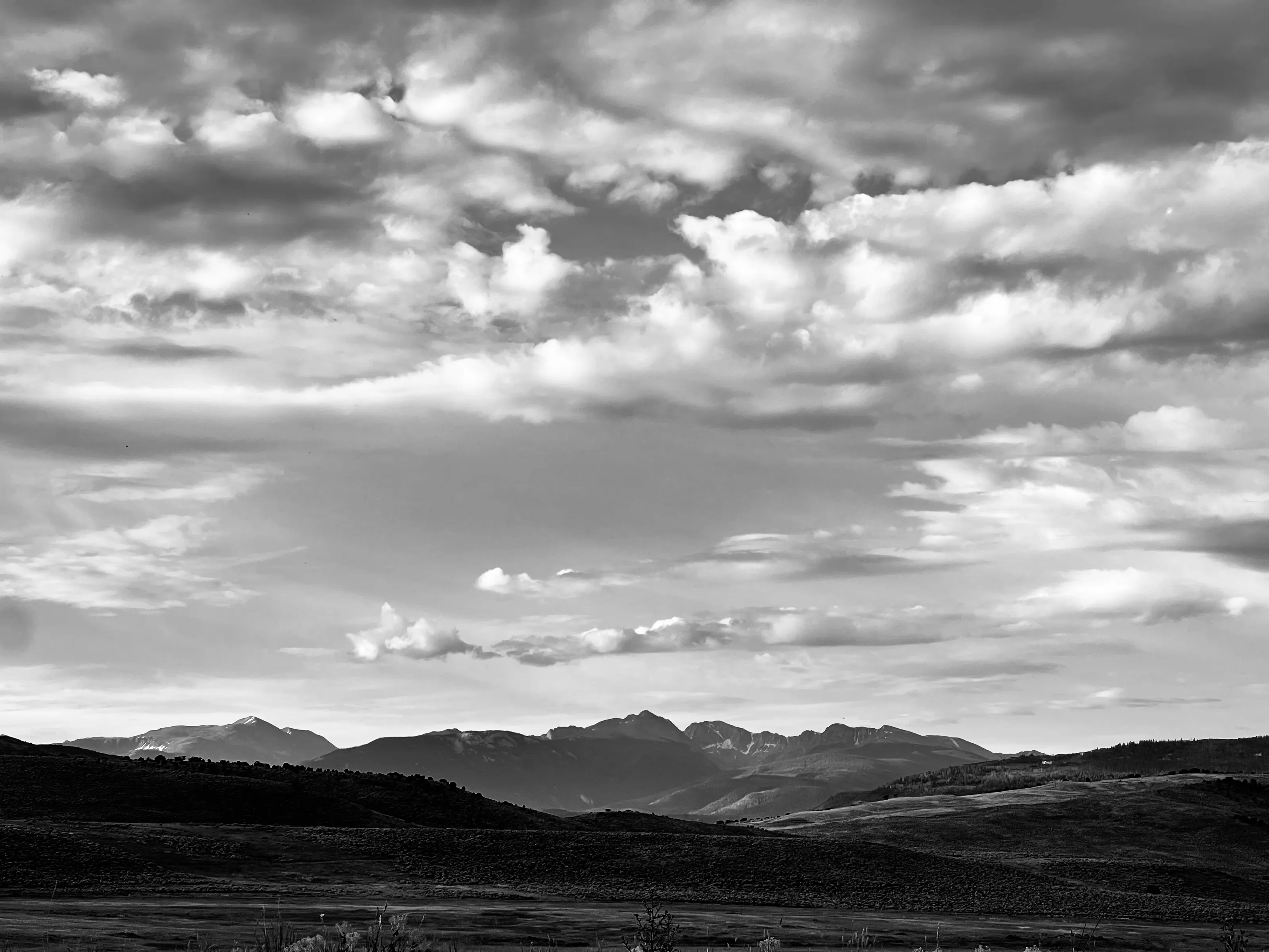 Black-and-white panoramic landscape of rolling dark hills, distant mountains, and layered clouds.