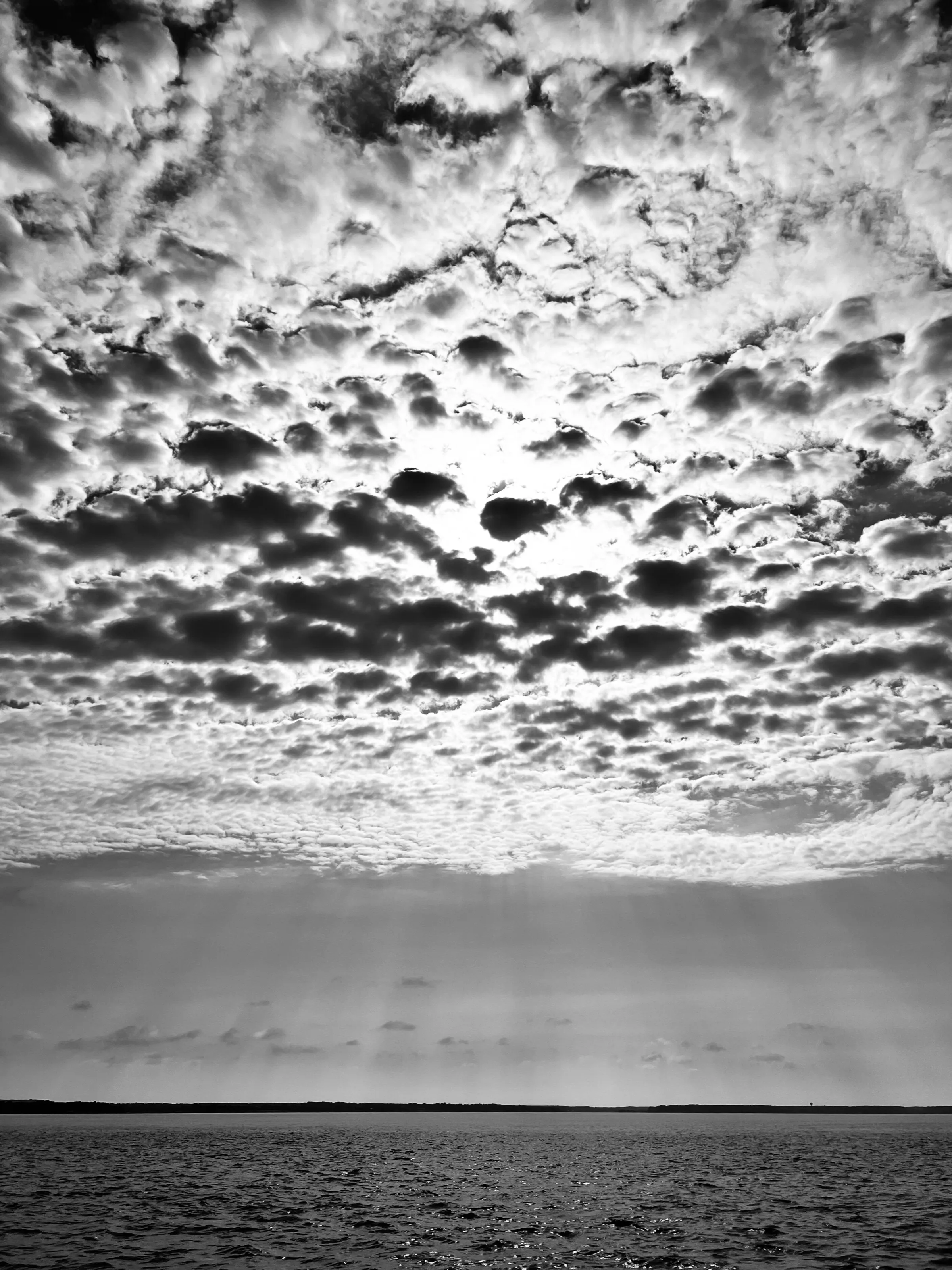 Dense black-and-white clouds fill the sky above a flat horizon and open water.