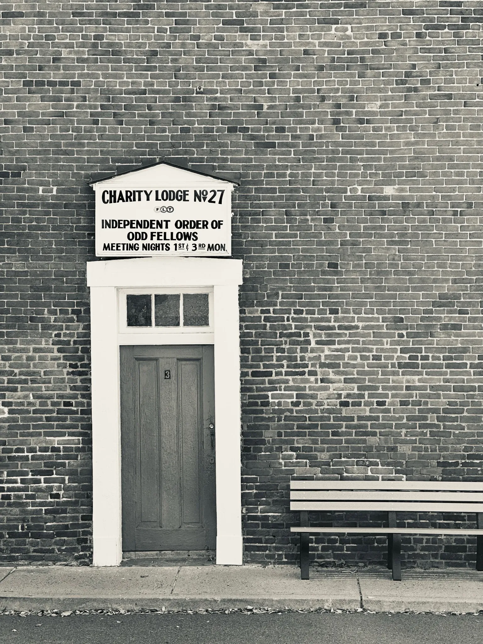 A gray door beneath a lodge sign beside a wooden bench against a large brick wall.