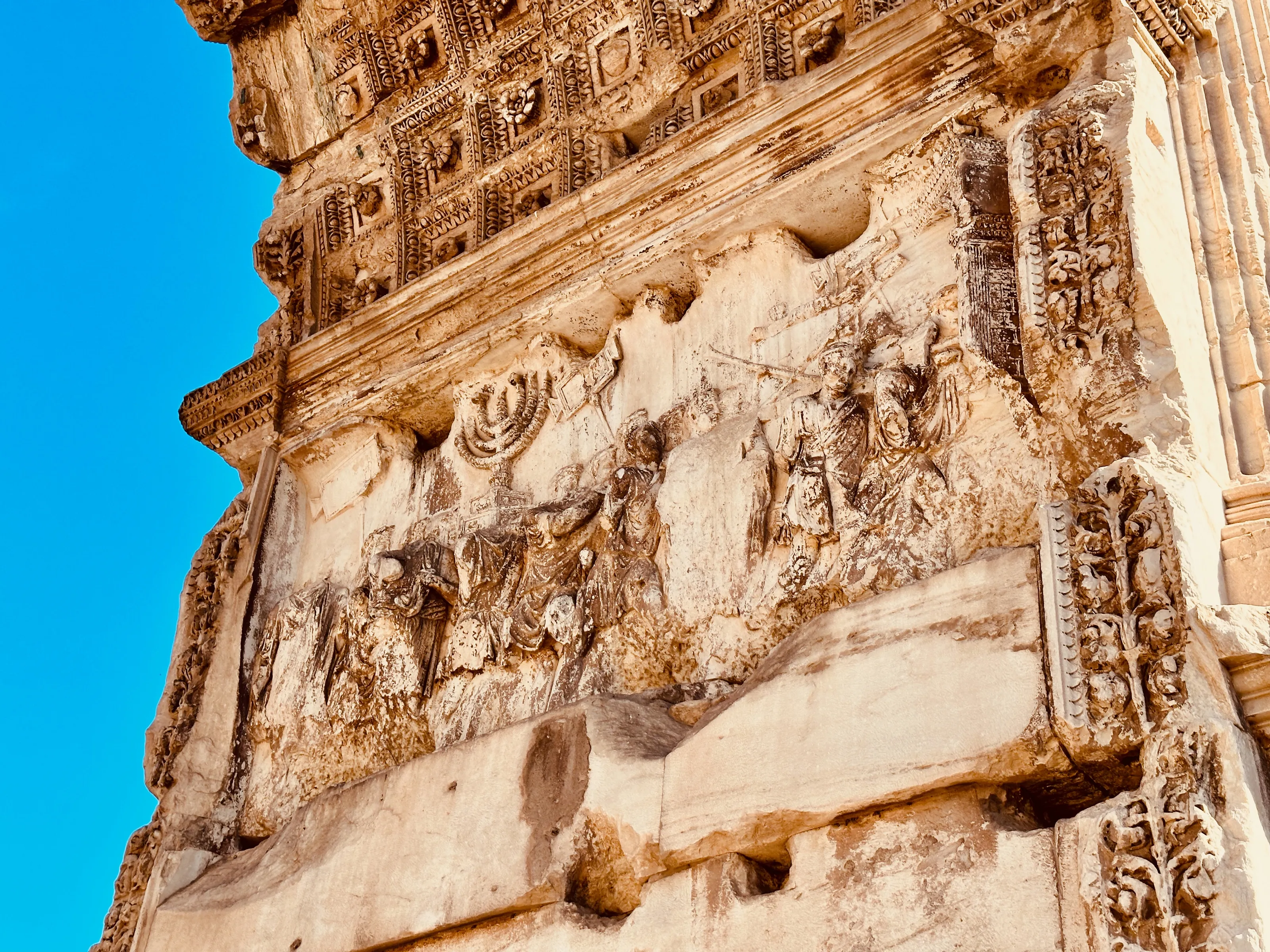 Close view of weathered carved stone figures and architectural ornament against a bright blue sky.