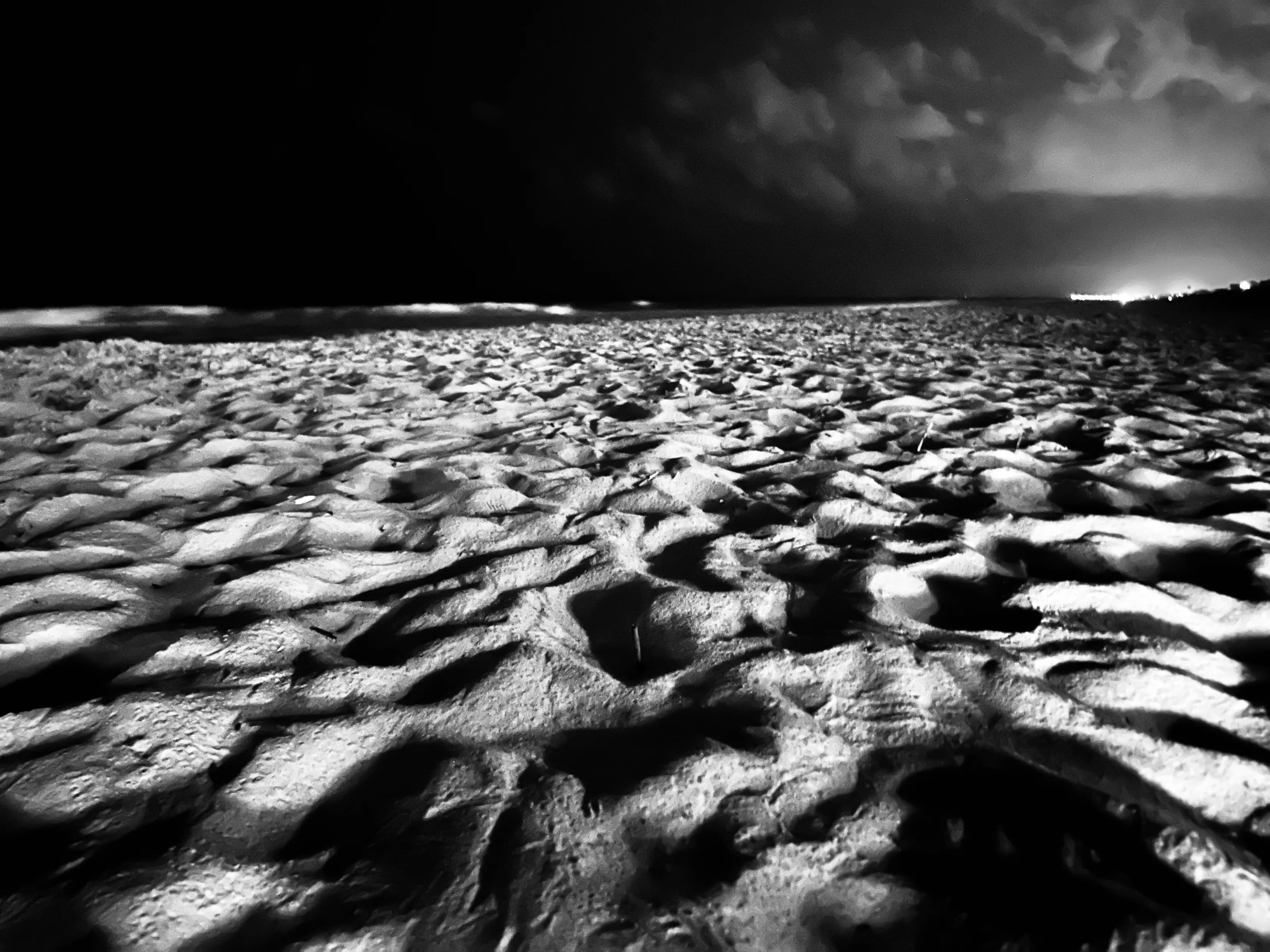 Rippling sand fills the foreground beneath dark storm clouds in a high-contrast black-and-white landscape.