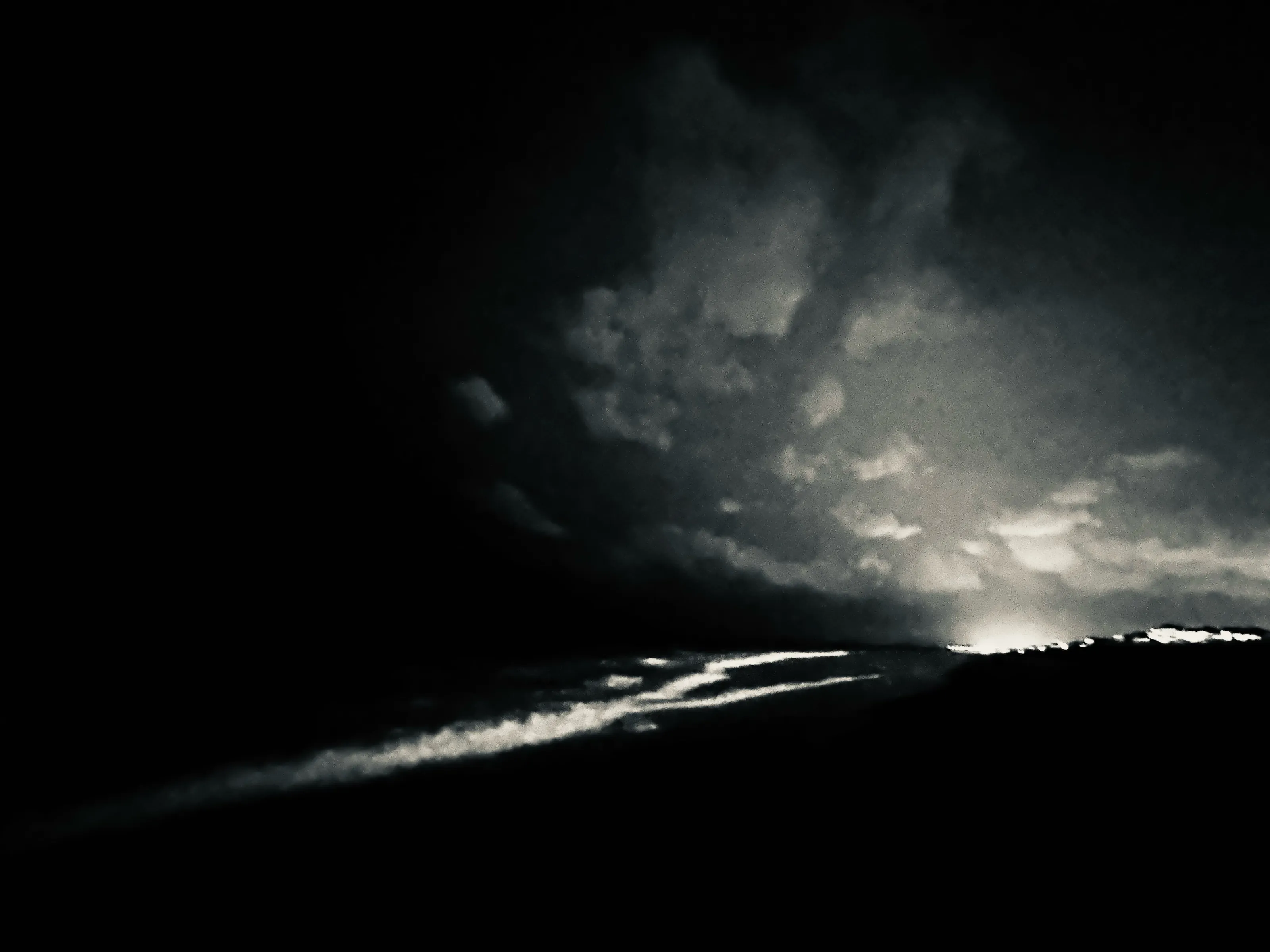 A dark black-and-white scene with clouds and streaks of light above a reflective surface.
