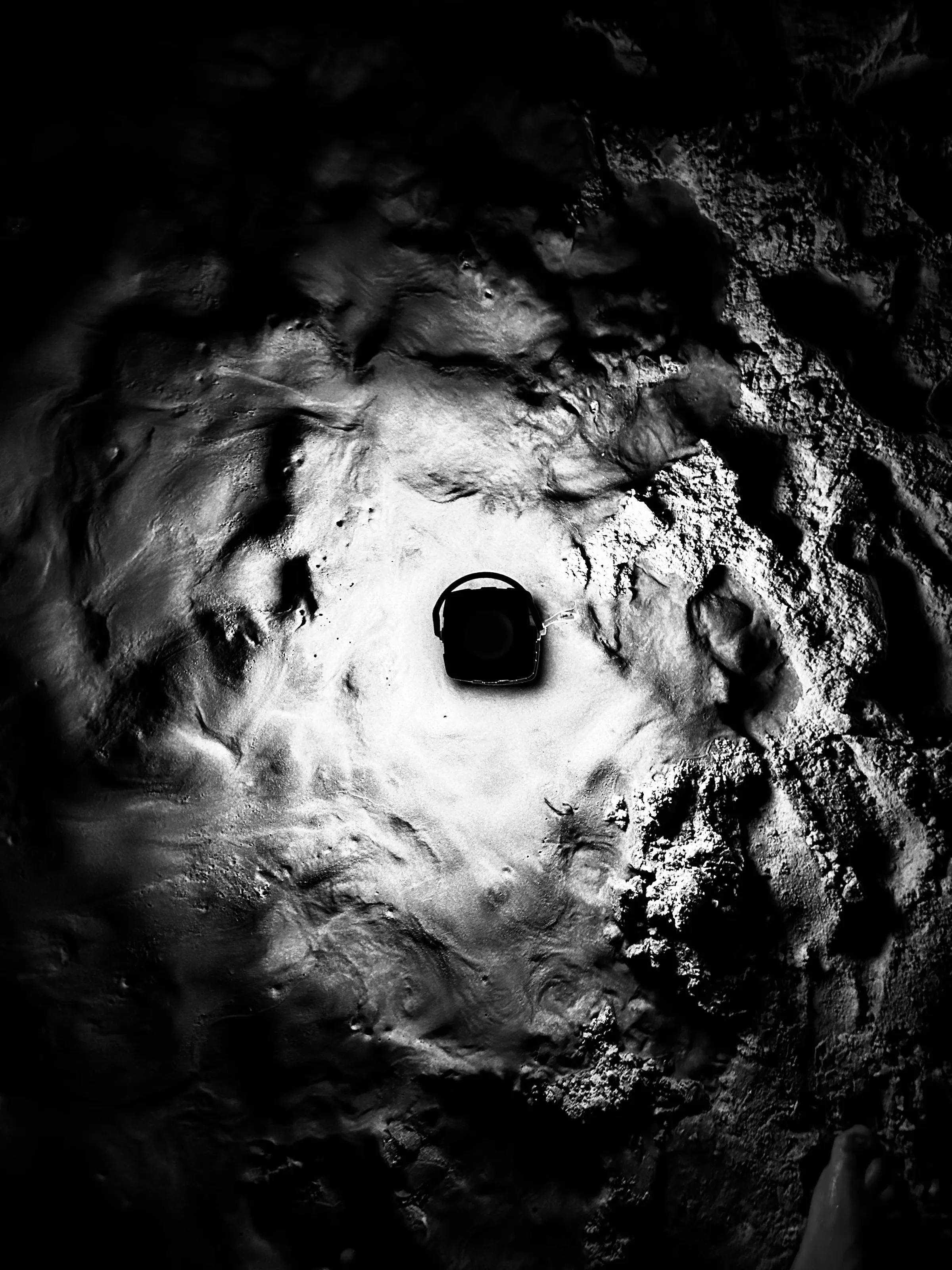 Black-and-white overhead photograph of swirling water or wet texture surrounding a dark square drain opening.
