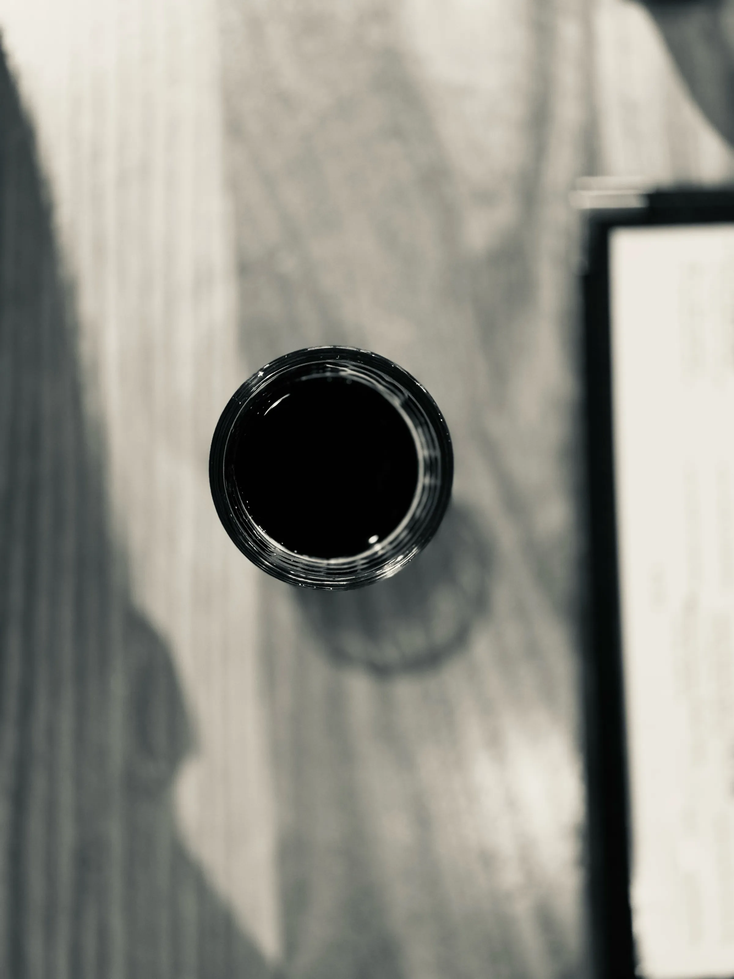 A top-down view of a dark drinking glass on a pale table, with a rectangular object at the right edge.