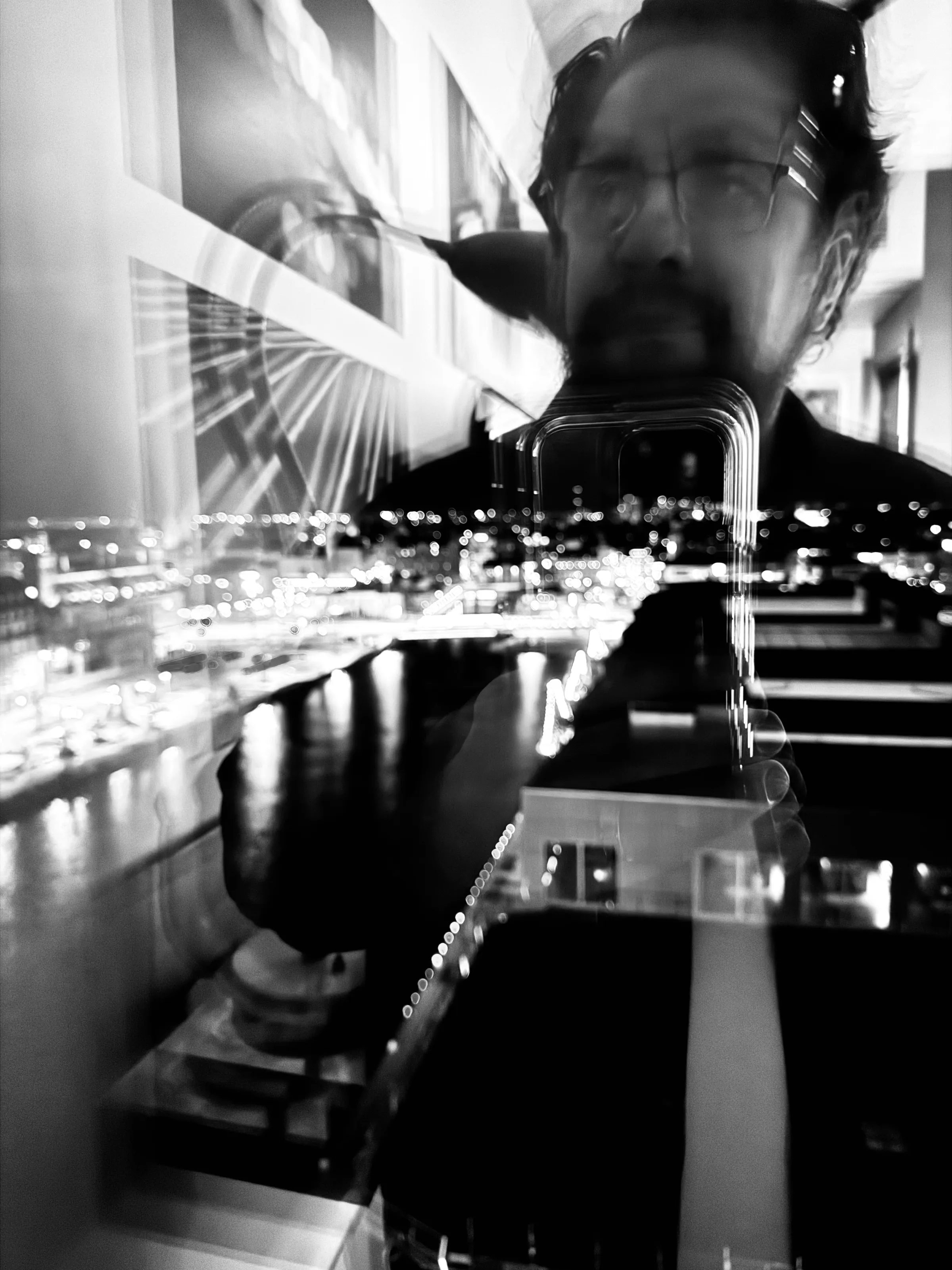 A blurred man with glasses appears in a reflection layered over night city lights and interior lines.