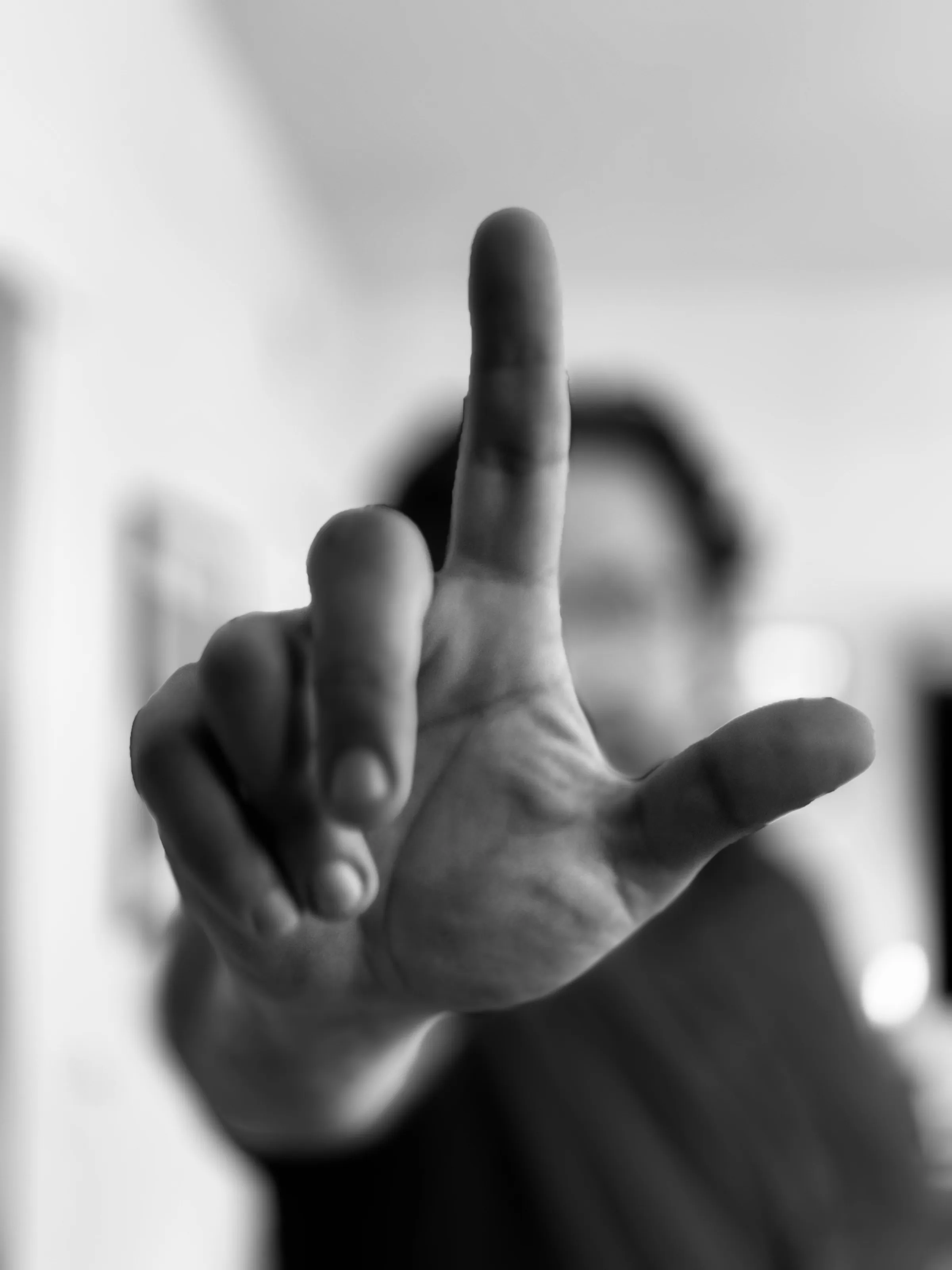 Black-and-white close-up of a person’s raised hand, with their face blurred in the background.
