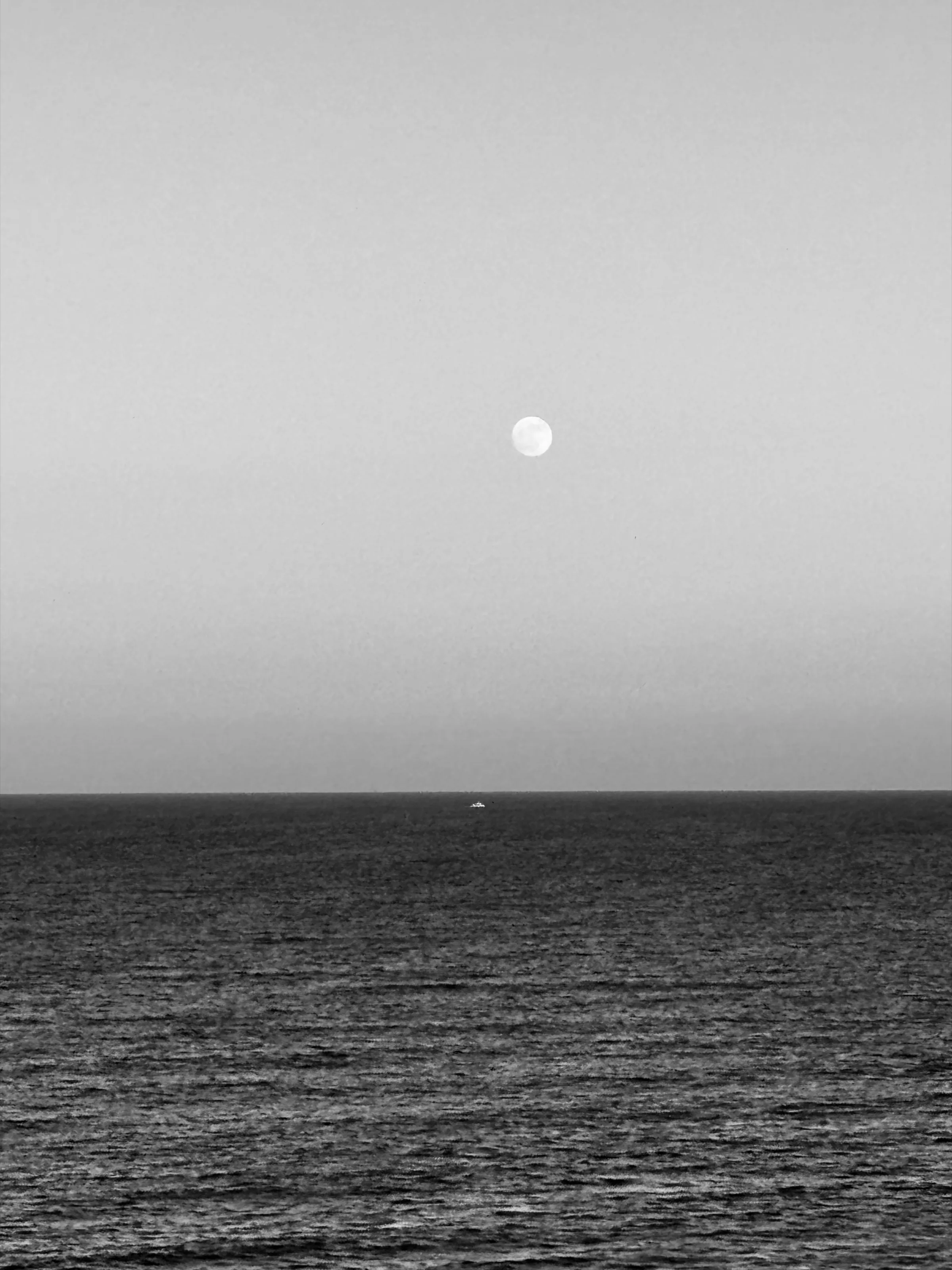 Black-and-white minimalist seascape with a pale moon above a dark horizon and a tiny boat in the distance.