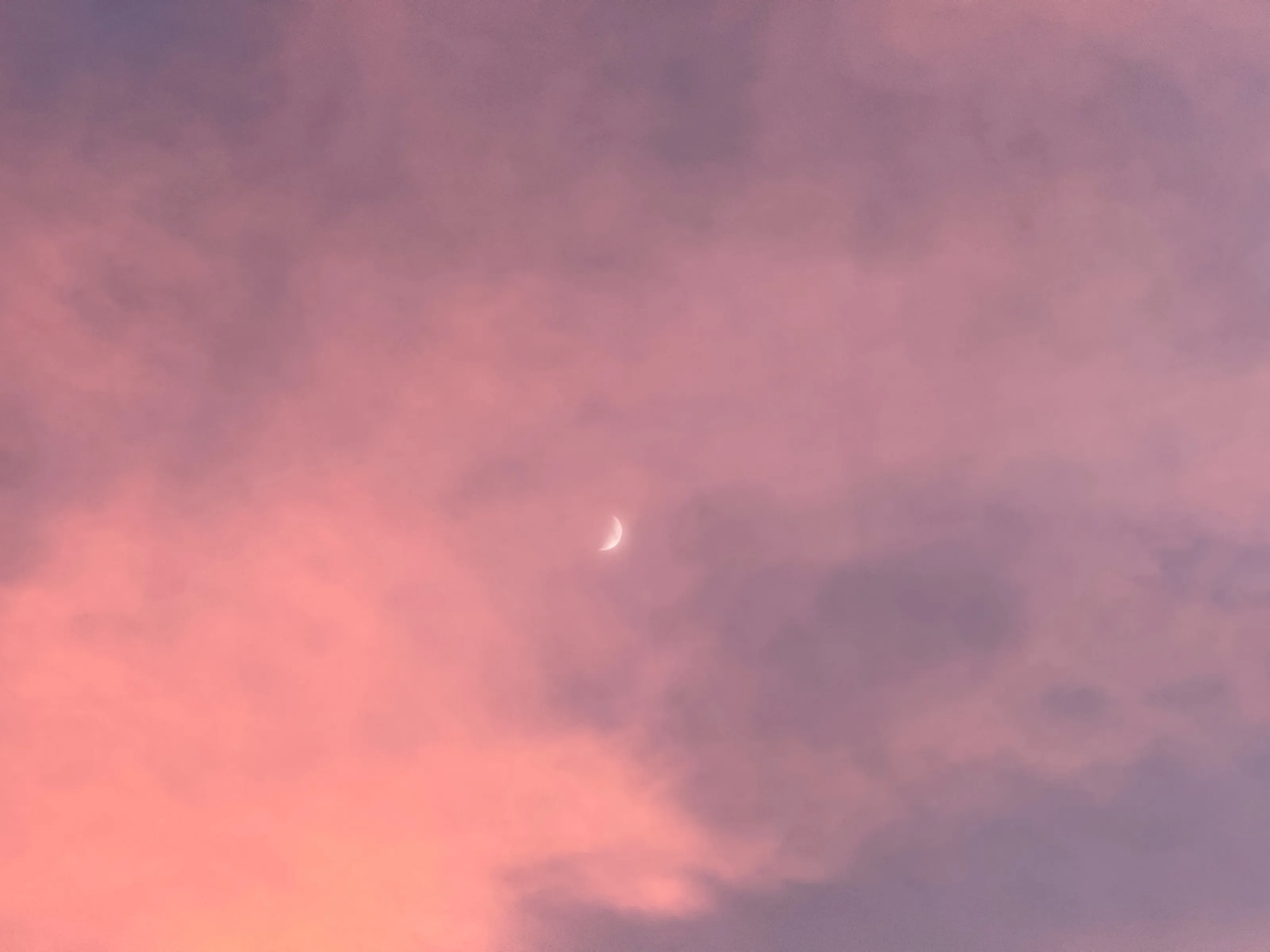 A small crescent moon appears among pink and purple clouds at twilight.