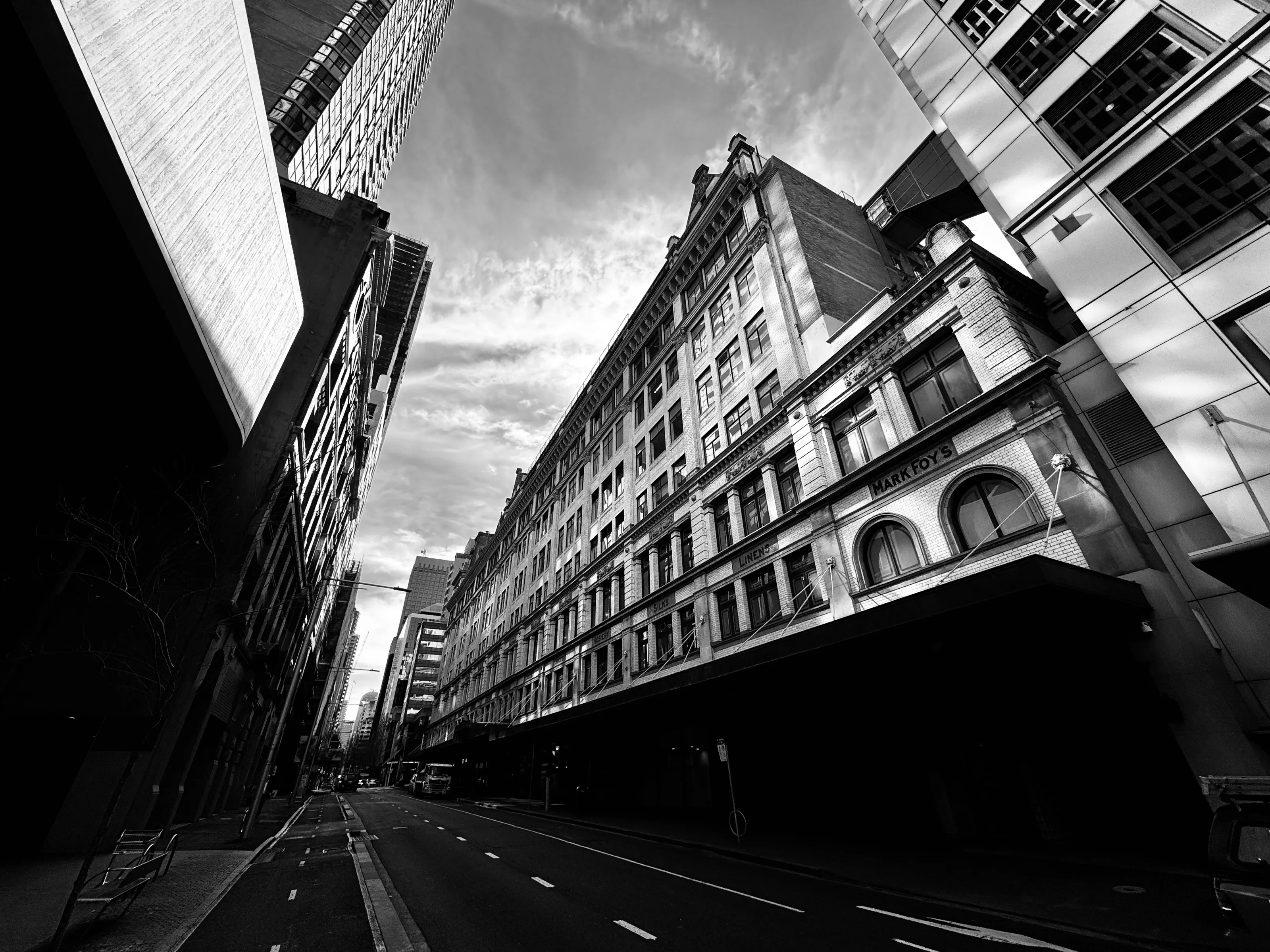 Black-and-white low-angle view along an empty city street lined with tall historic and modern buildings.