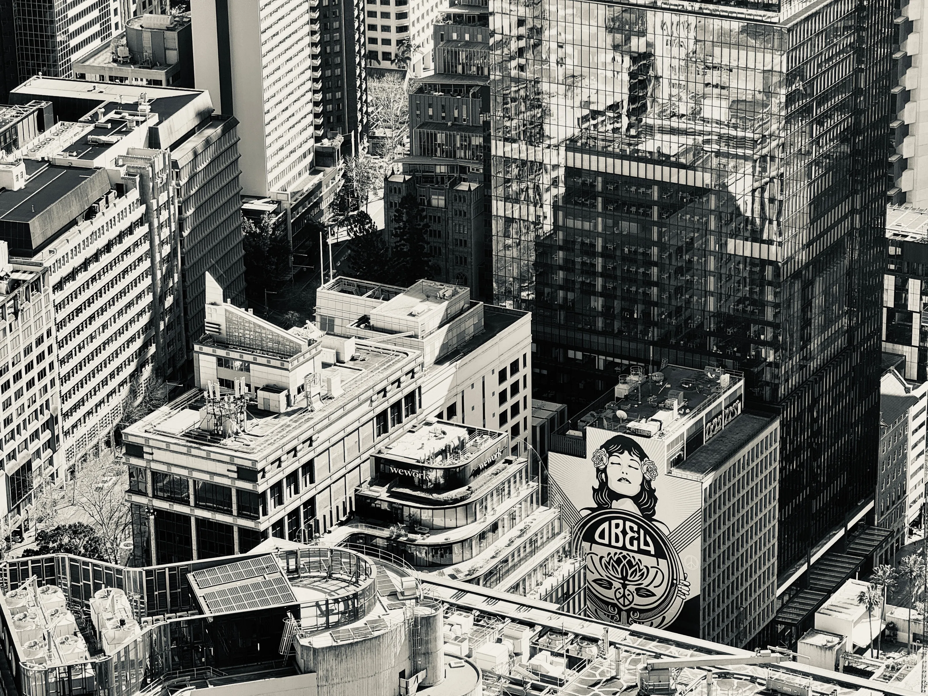 Black-and-white aerial view of dense downtown buildings, rooftops, reflected glass, and a large mural on one wall.