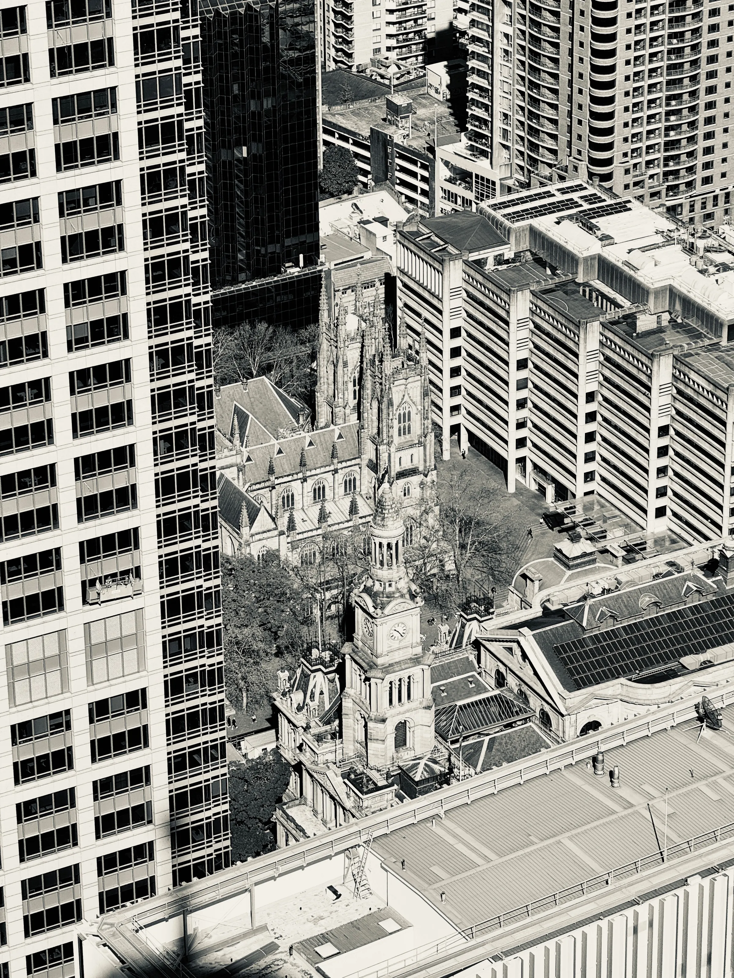 A historic stone church and clock tower sit tightly between modern high-rise office and apartment buildings.