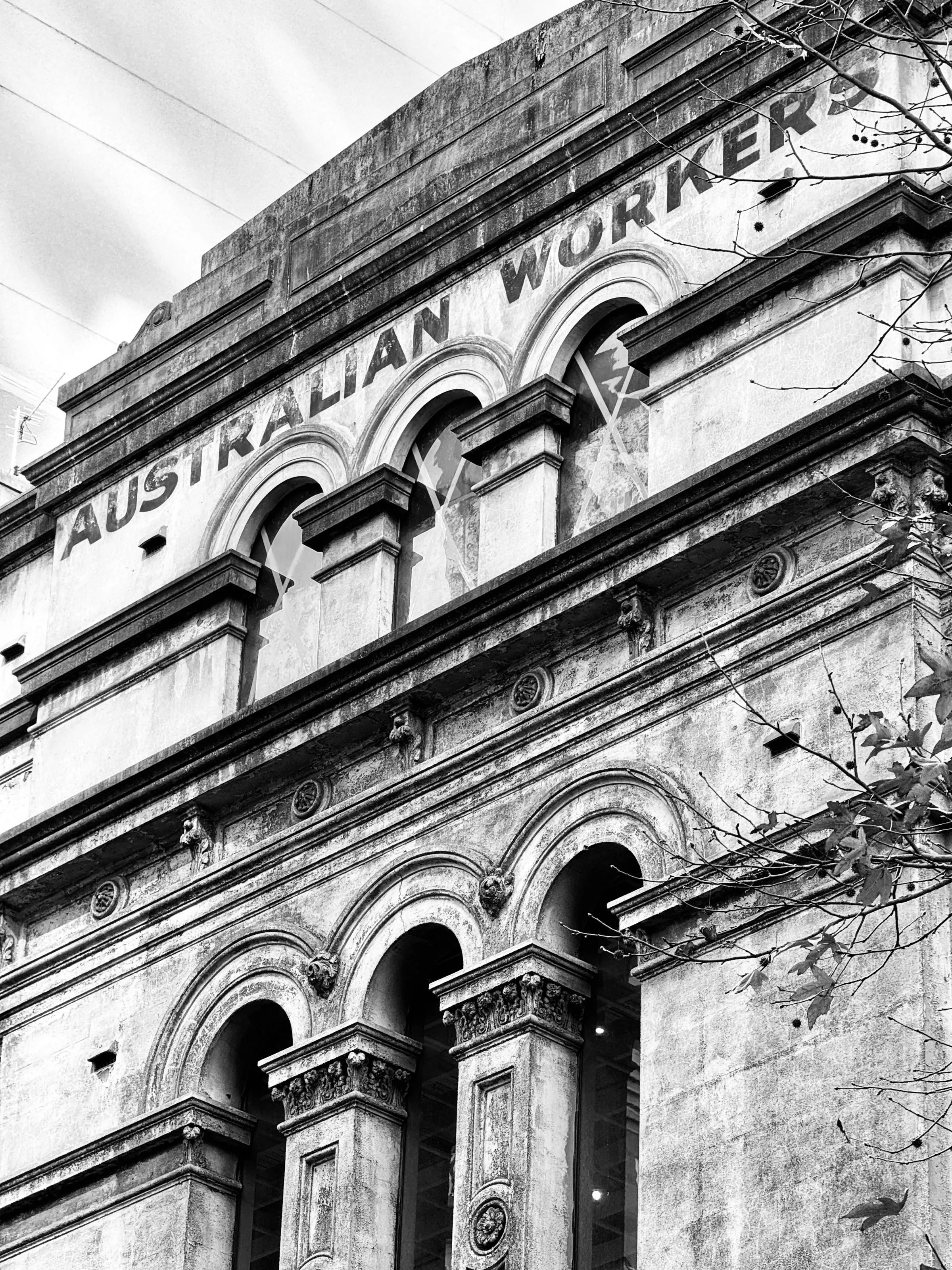 A weathered historic building facade with arched windows bears the words Australian Workers near its roofline.