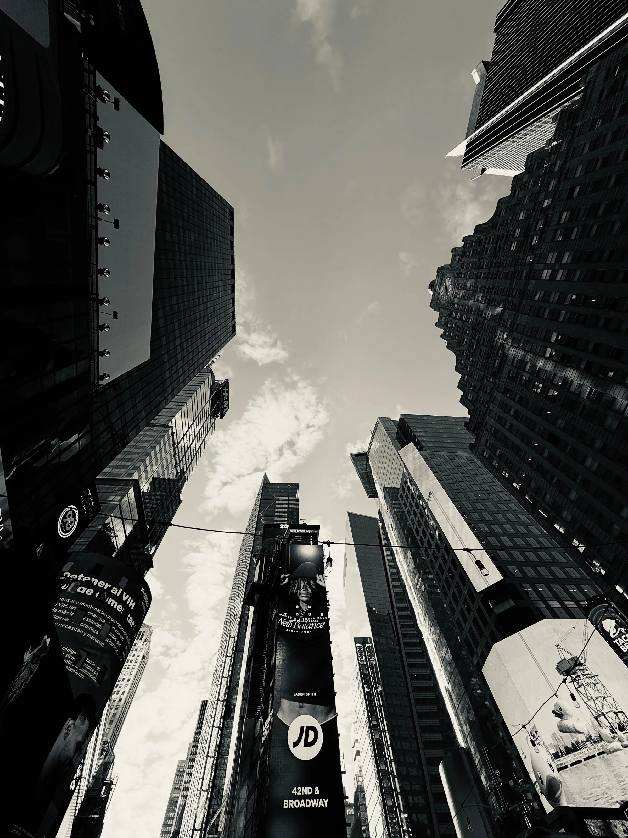 Black-and-white upward view between tall city buildings and billboards.
