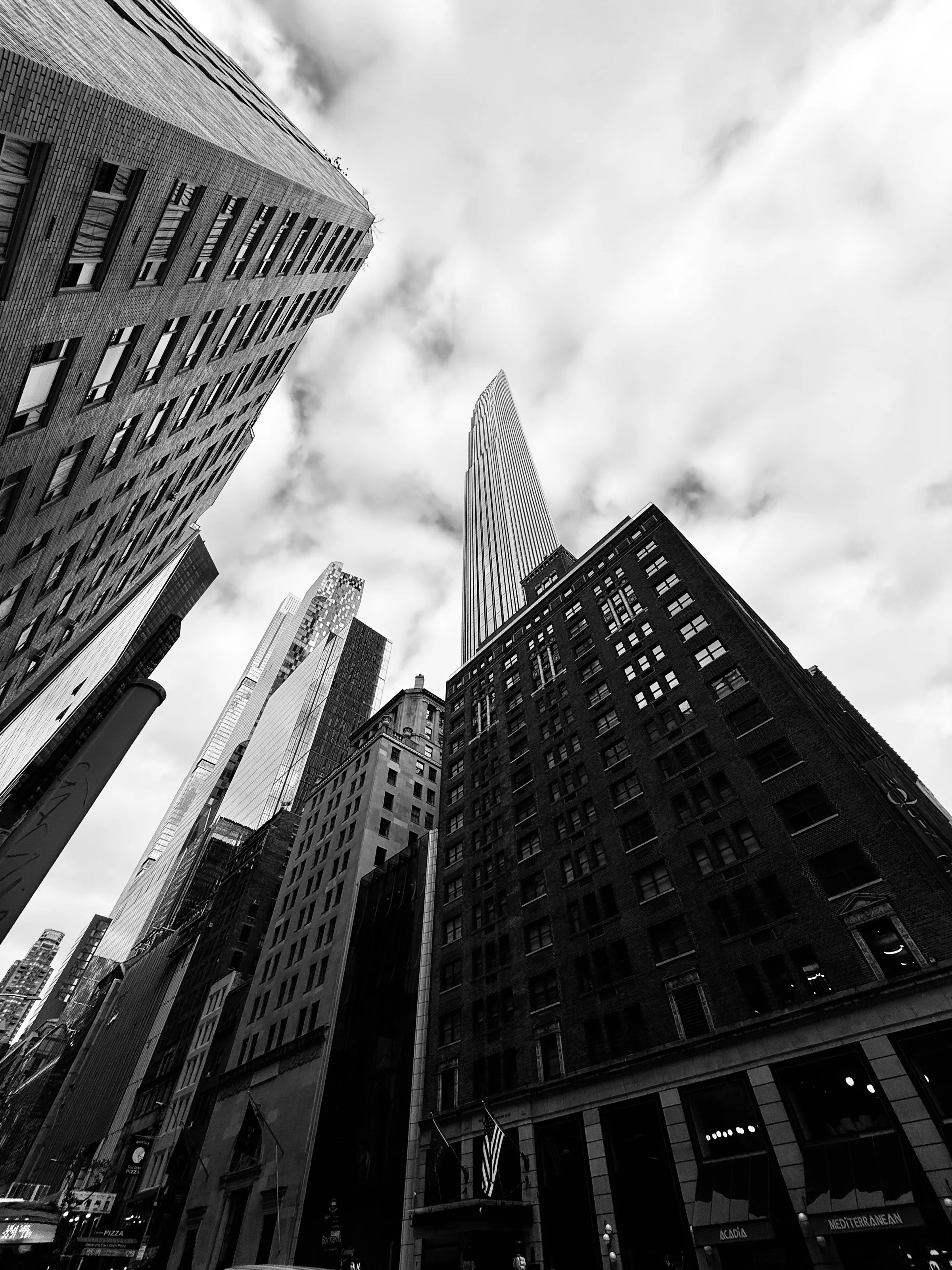 Black-and-white upward view of tall buildings along a narrow city street.
