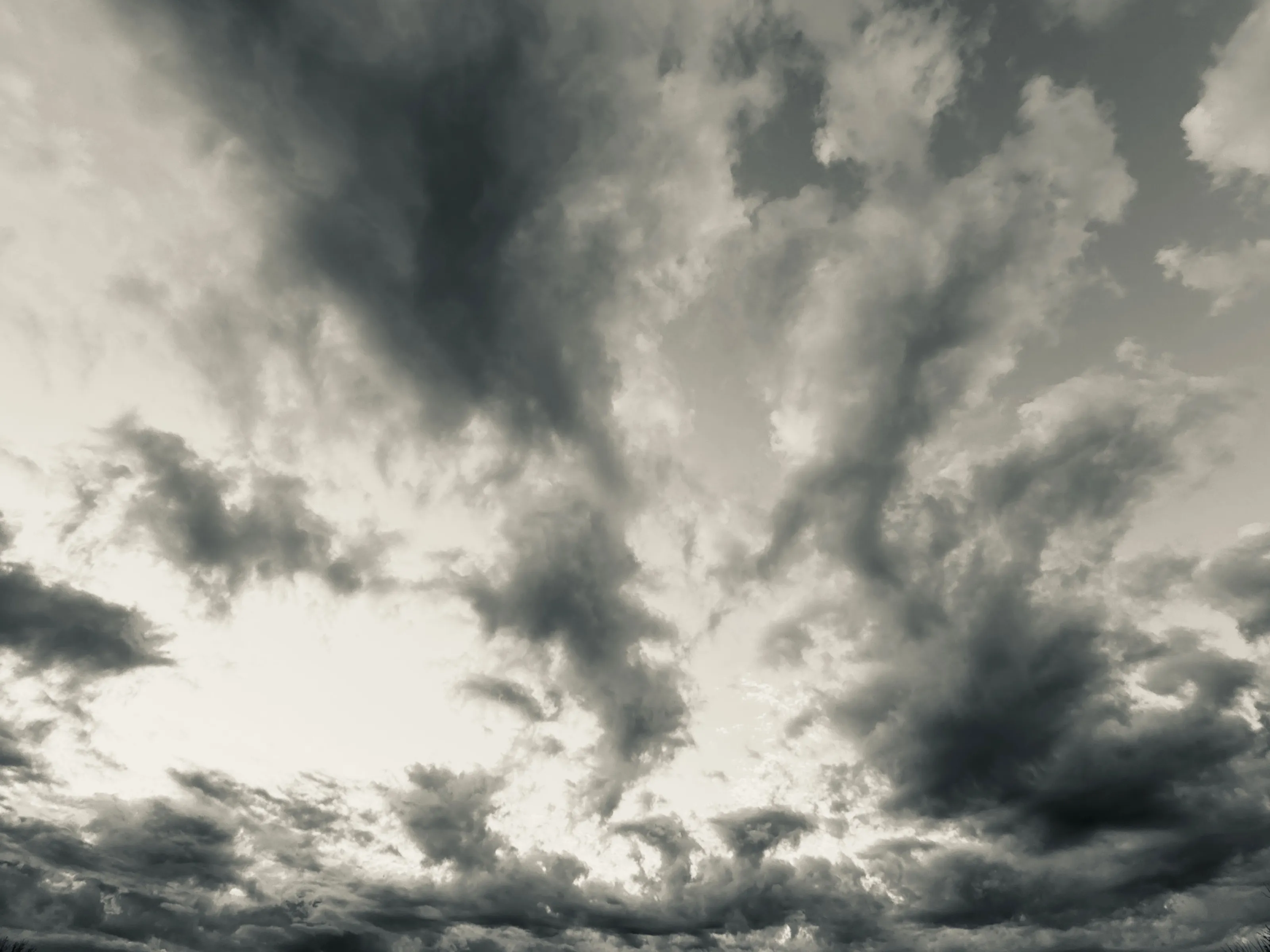 Black-and-white photograph of layered dark storm clouds with a bright opening near the horizon.