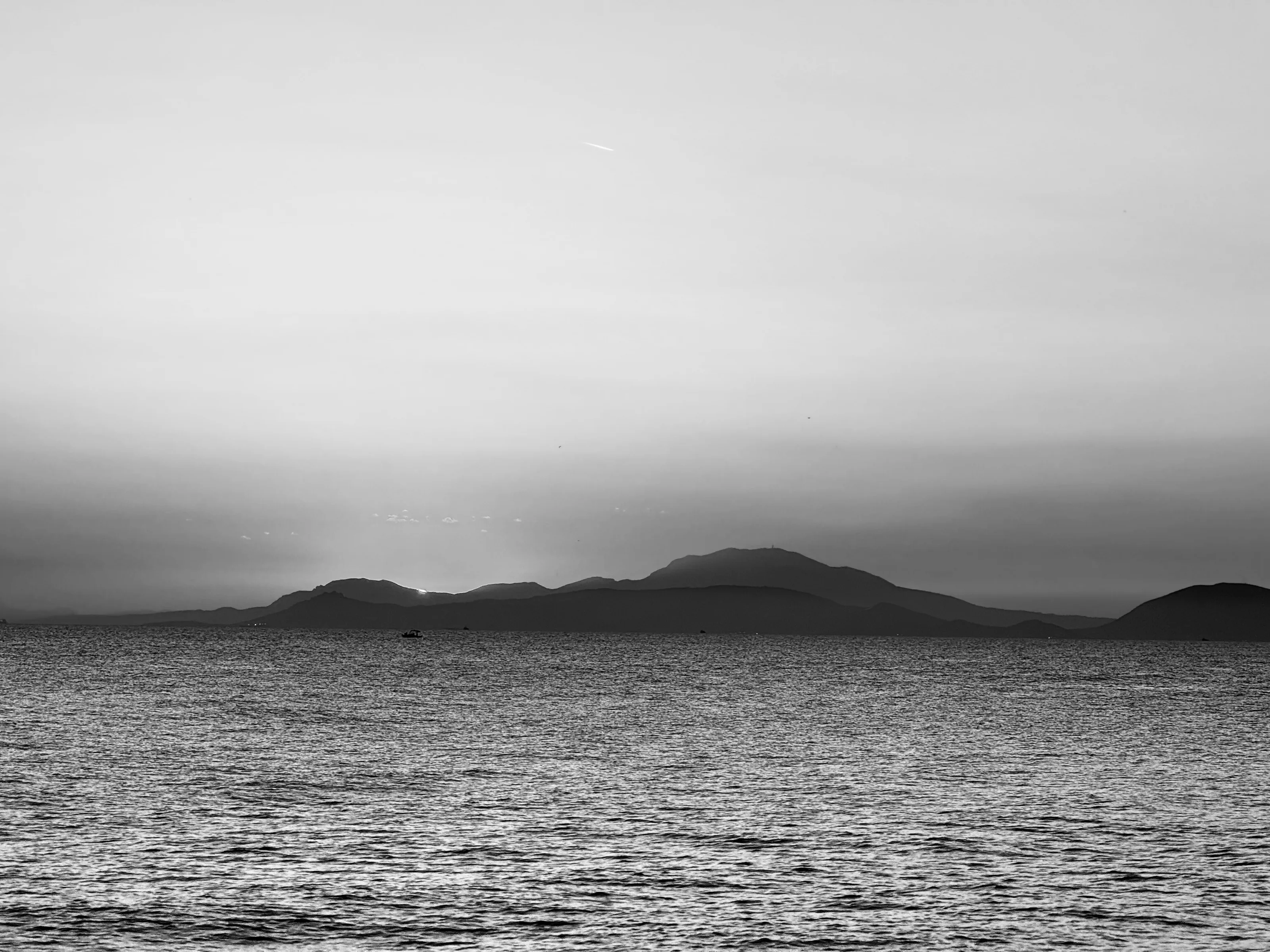 Black-and-white view of rippled water and dark low islands beneath a pale sky.